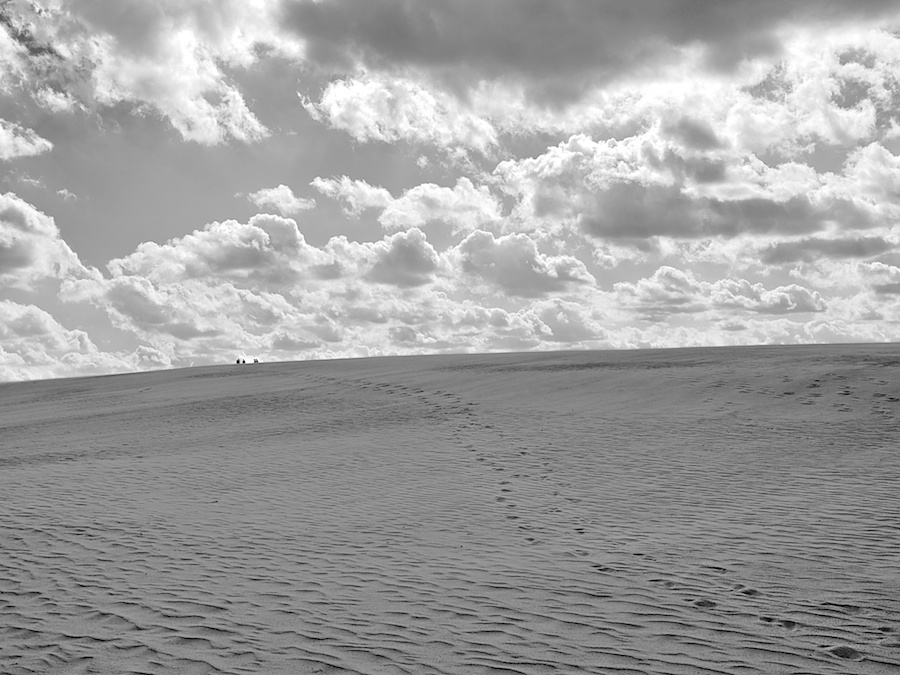 Dune footsteps leading to people on a faraway horizon.