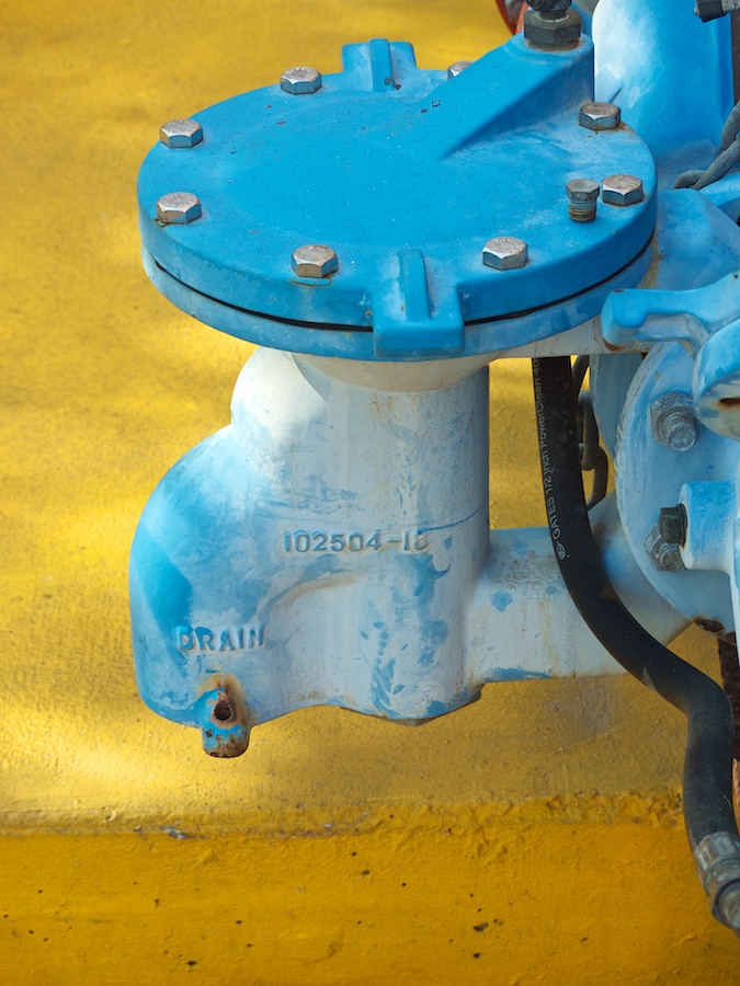 Blue drain mechanism against yellow pavement.