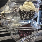 Cupcakes in plastic containers on bar towel.