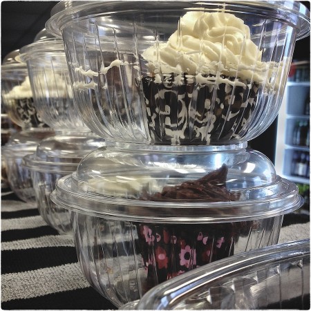 Cupcakes in plastic containers on bar towel.