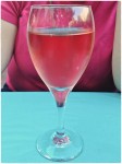 Glass of white zinfadel on turquoise tablecloth with fuschia shirt behind.