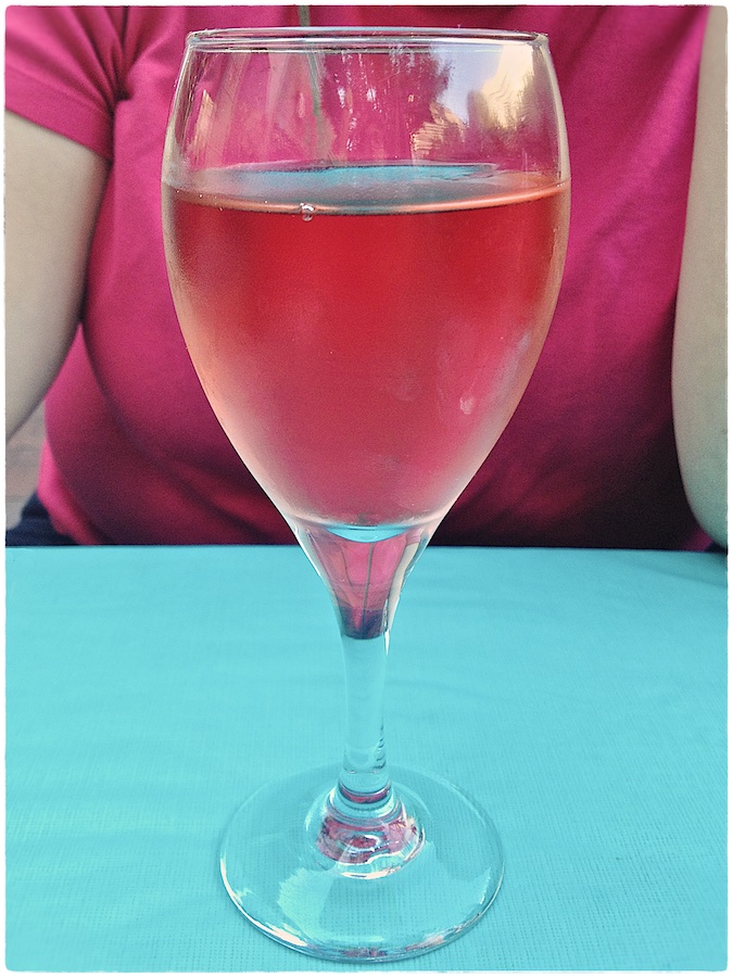 Glass of white zinfadel on turquoise tablecloth with fuschia shirt behind.