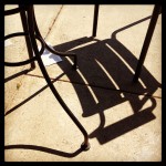Outdoor furniture shadows on sidewalk.