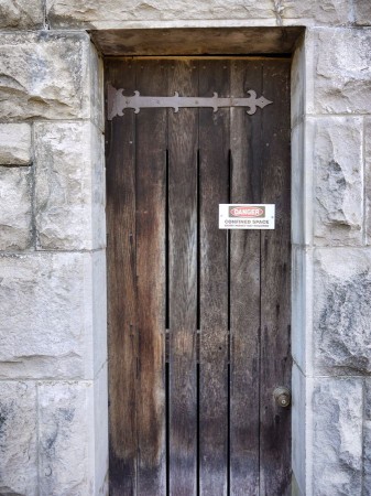Narrow wooden door in stone wall with danger sign.